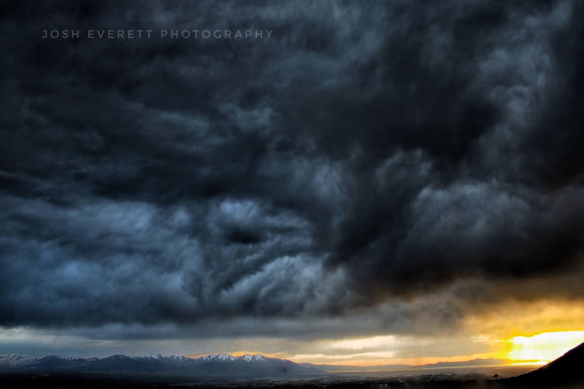 Dark and heavily textured clouds with A golden sky and mountains in the background.