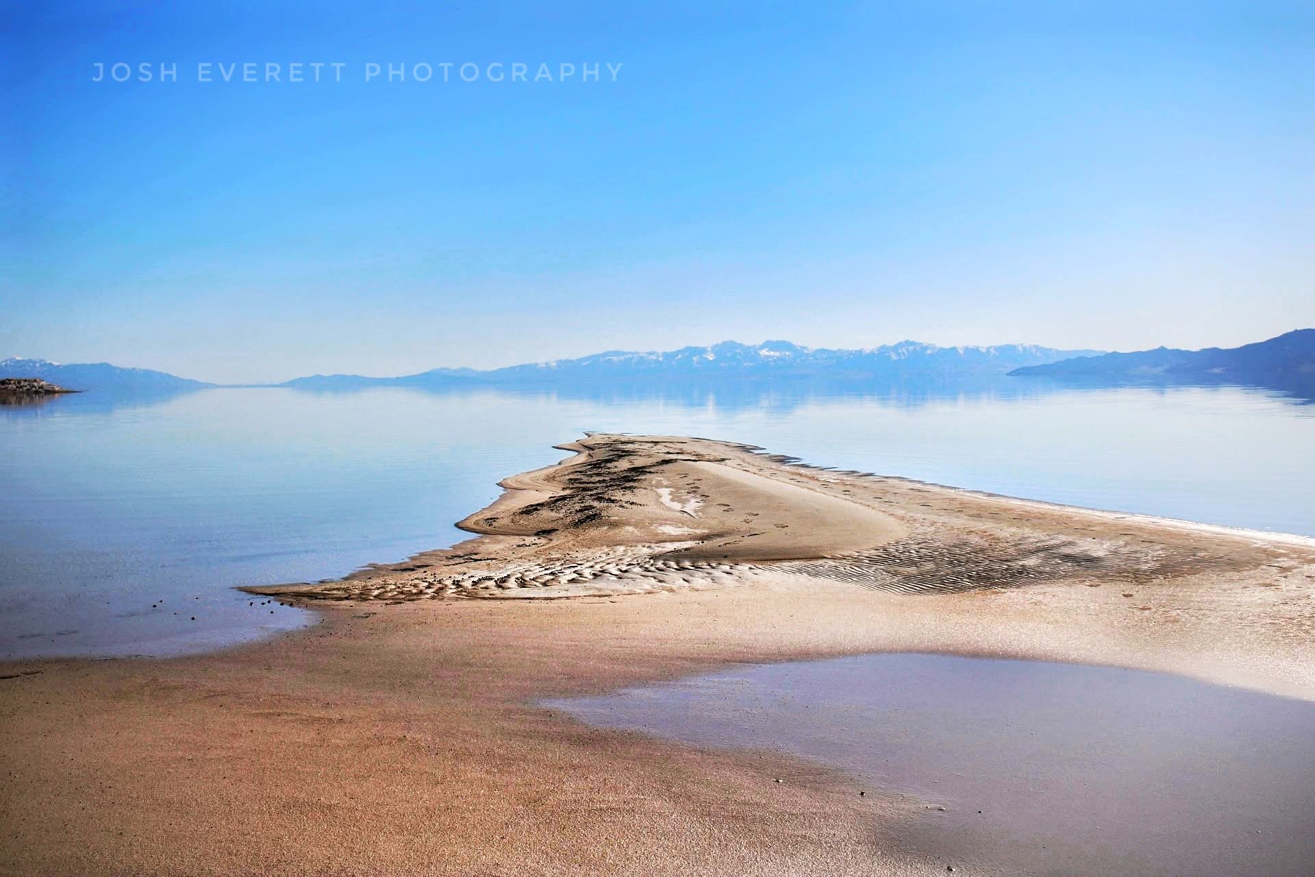 Angular sand bank with a lake that makes the mountains look like they are floating in the sky.
